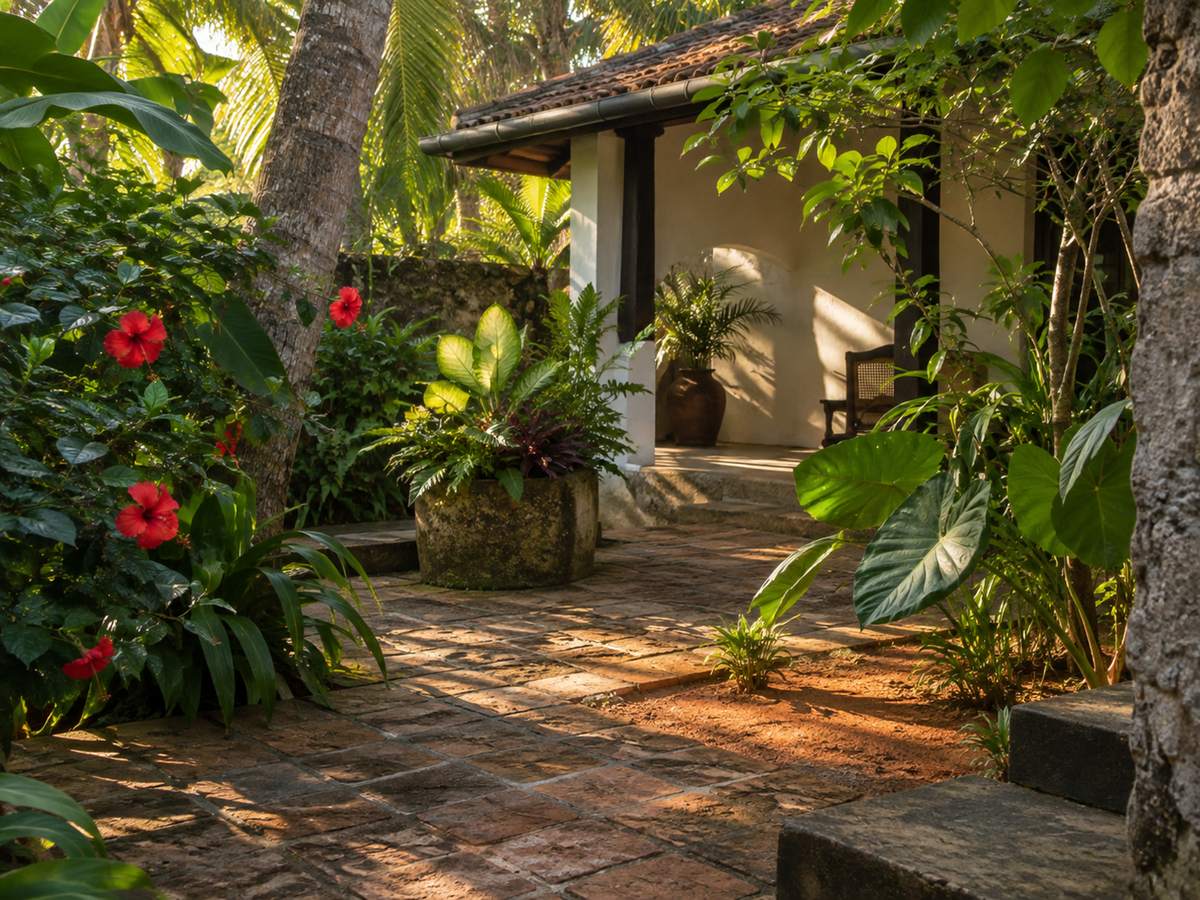 Late-afternoon garden courtyard with coconut-palm shade, clay tiles and a gold-hour patch of laterite